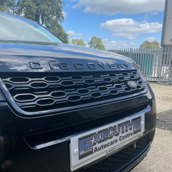 Front of a black Land Rover Discovery in an outdoor setting with a clear sky and trees.