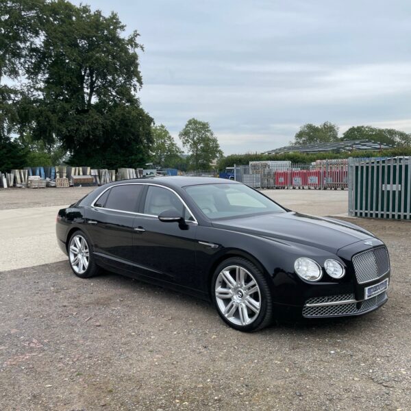 Black luxury sedan parked on gravel with an industrial background.
