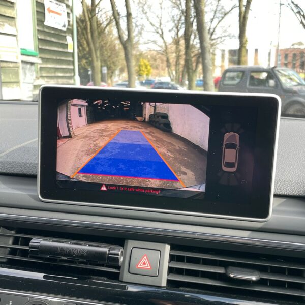 Car dashboard with reverse camera display showing driveway.