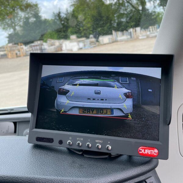 Vehicle dashboard with a rear-view camera screen showing the back of a white car with parking guide lines.