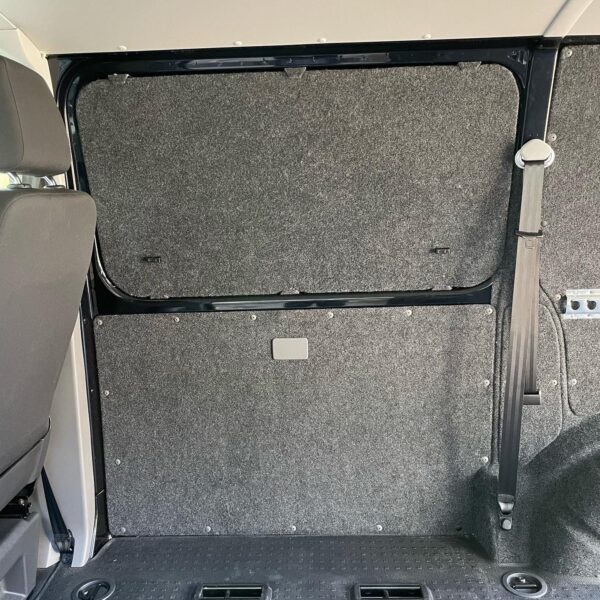 Interior side panel of a van with gray felt covering and a seatbelt.