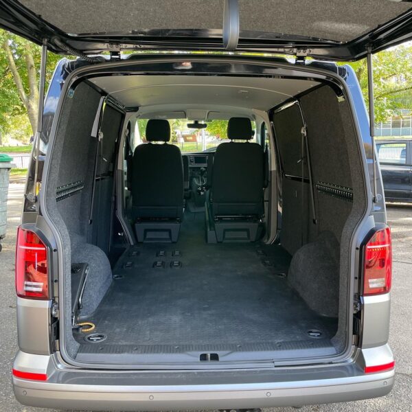 Interior of an empty gray van viewed from the rear, showing carpeted cargo space and front seats.