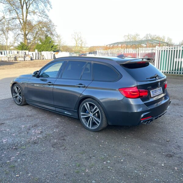 A dark gray BMW station wagon parked on a gravel surface with a clear sky background.