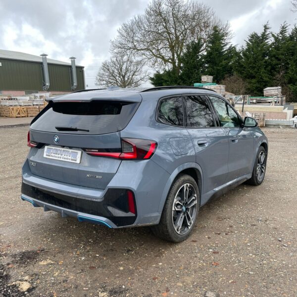 Gray BMW SUV parked on gravel under a cloudy sky.