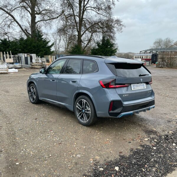 A gray BMW SUV parked on gravel, with trees and construction materials in the background.