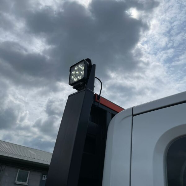 Industrial spotlight on a vehicle against a cloudy sky backdrop.