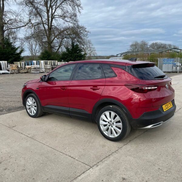 Red SUV parked on a concrete surface with cloudy sky and trees in the background.
