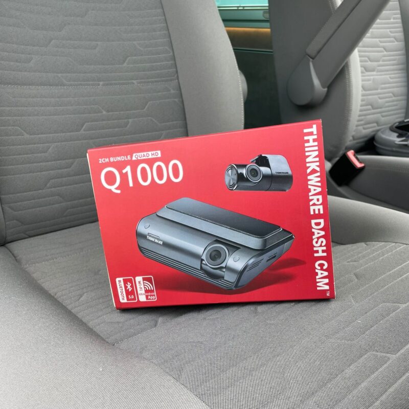 A red Thinkware Dash Cam box labeled "Q1000" on a grey car seat.