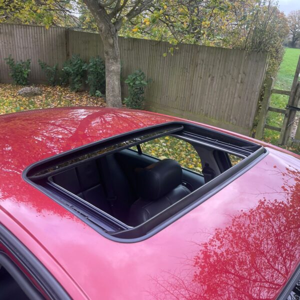 Open sunroof of a red car with trees and a wooden fence in the background.