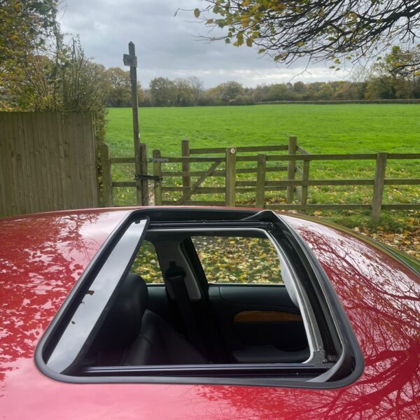 Open sunroof of a red car with a field and cloudy sky in the background.