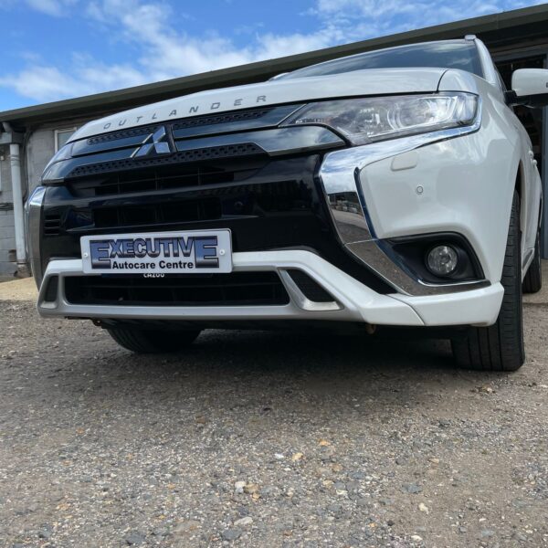 Front view of a white Mitsubishi Outlander on a gravel surface with blue sky.