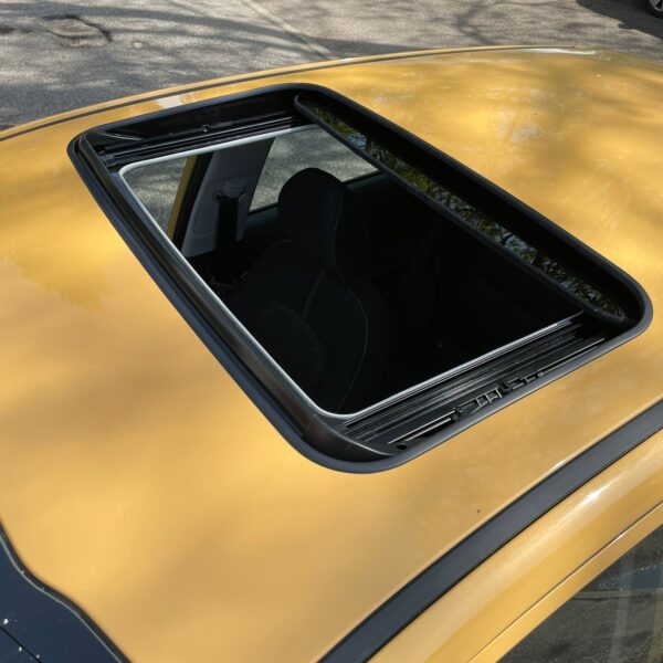 A yellow car with an open sunroof parked on a street.