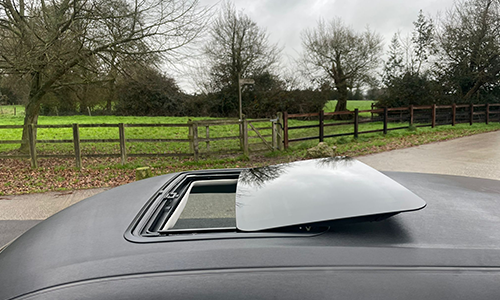 Partially open sunroof on a car with a rural landscape in the background.