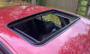 Open sunroof of a red car viewed from above, with reflections of autumn trees.